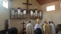 kerkelijke figuren voor het altaar van een kleine kerk met twee delen orgelpijpen en in het midden een groot kruis