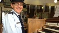 Een man in uniform met bril op die achter een kerkorgel zit in een kerk